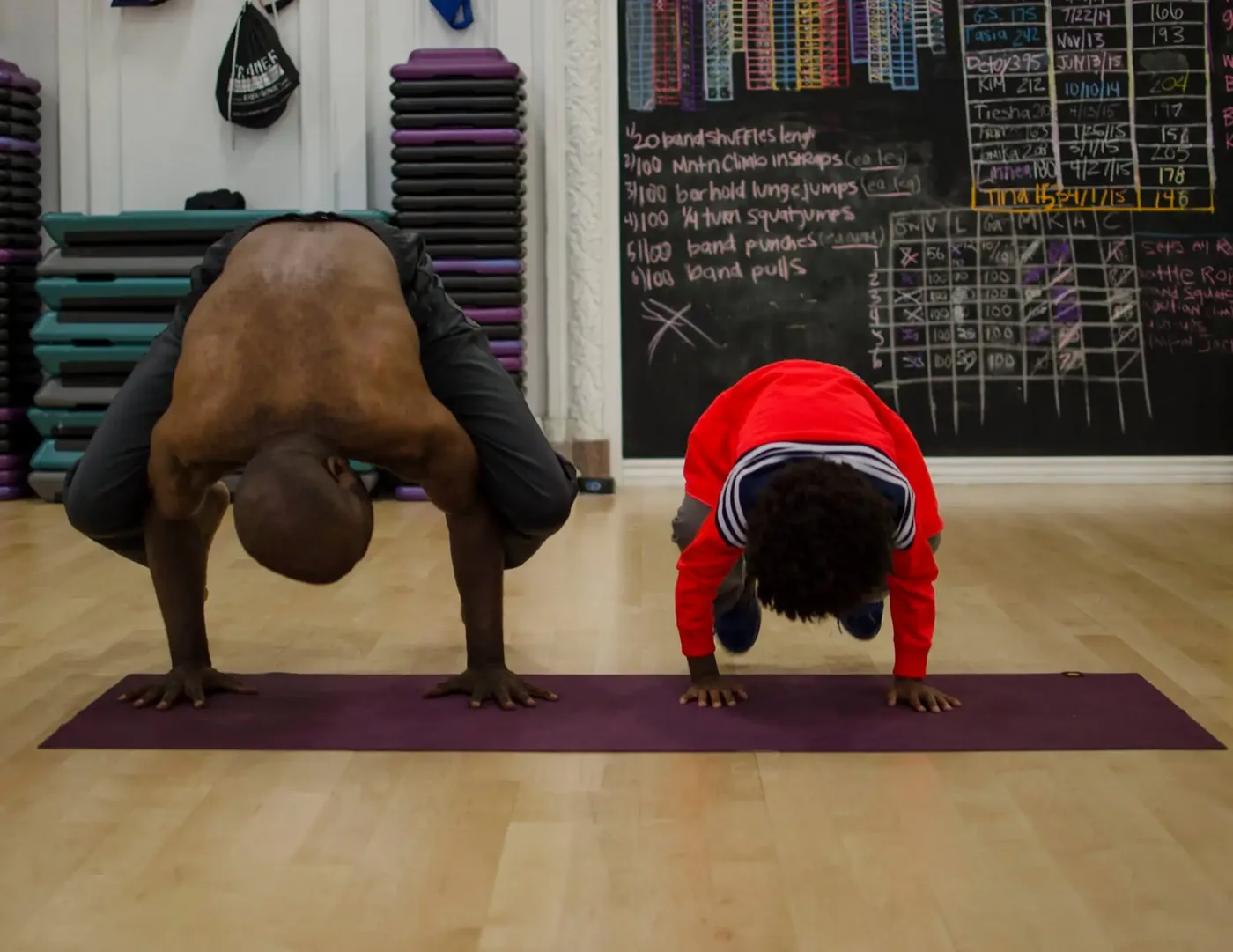 Akhu Ausar and a young student holding crow pose on yoga mats in the studio